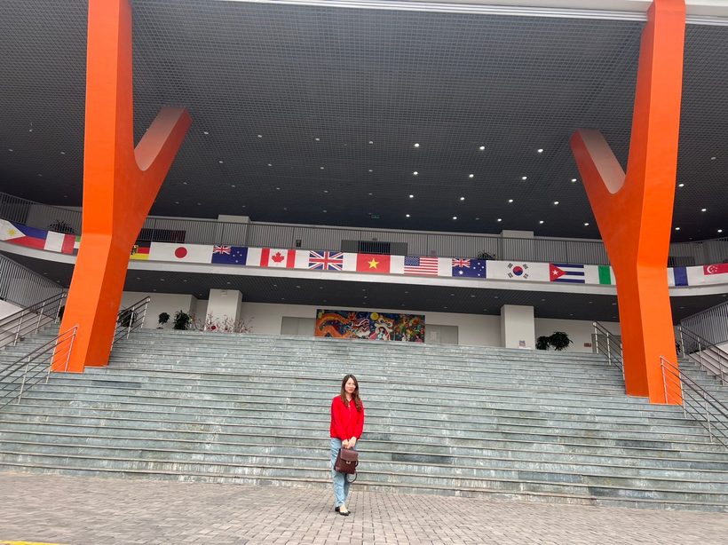 A person standing in front of a building with flagsDescription automatically generated